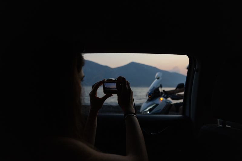 Woman photographing through a car window at dusk